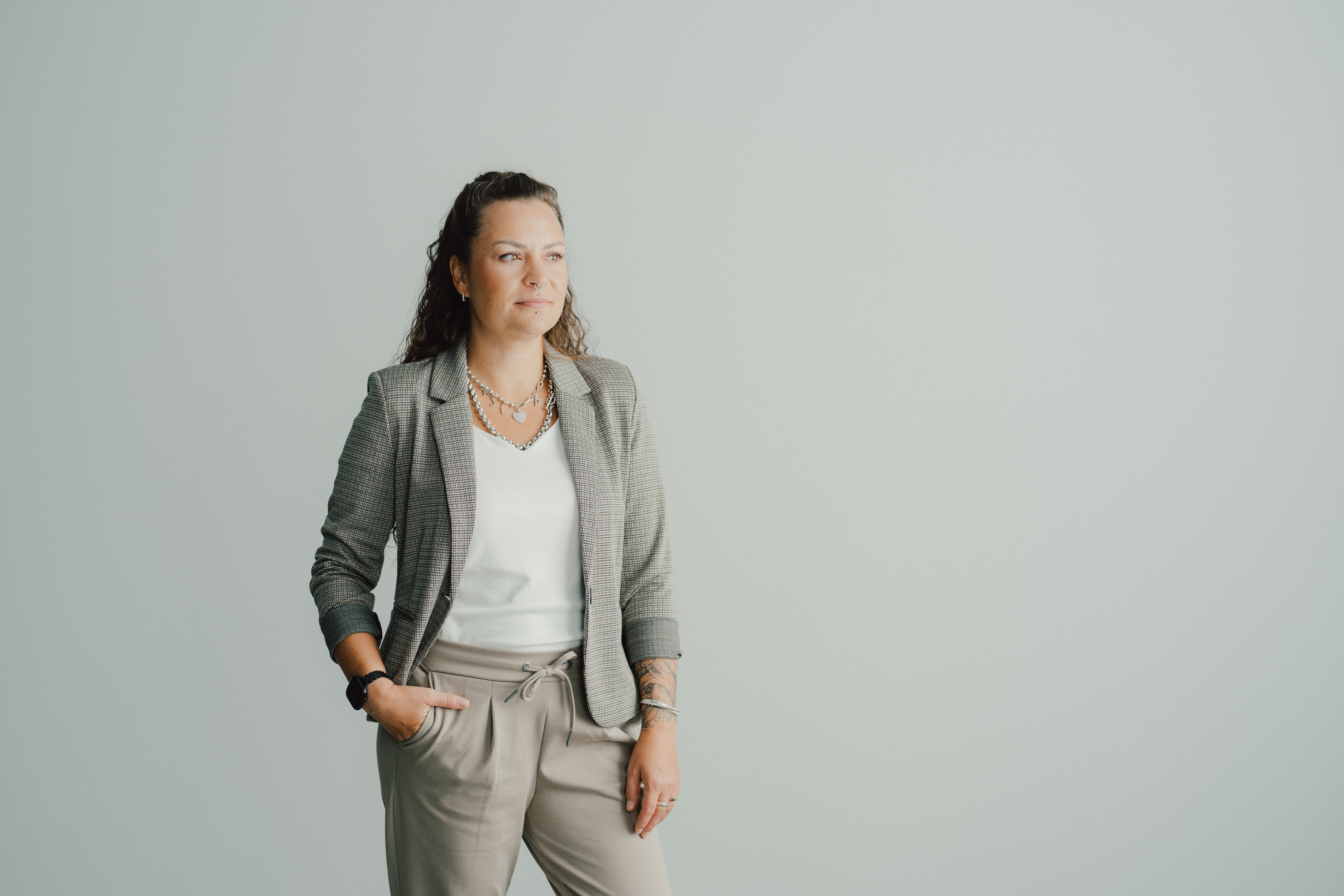 Kim-Nina Ernst im grauen Blazer, stehend vor einer weiten hellen Wand